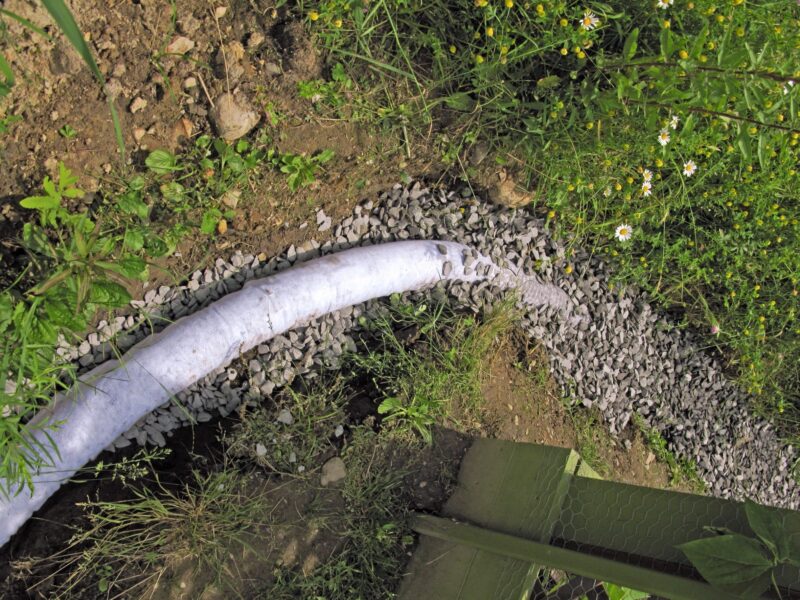 perforated pipe surrounded by gravel in a shallow yard trench to complete french drain installation project